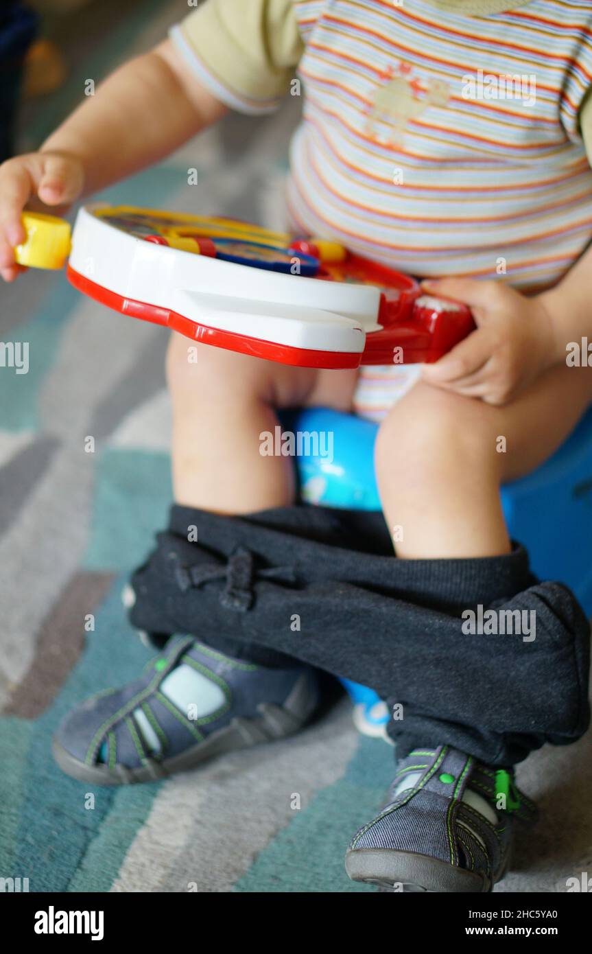 A young boy sitting on a potty while holding a farm sound toy Stock Photo