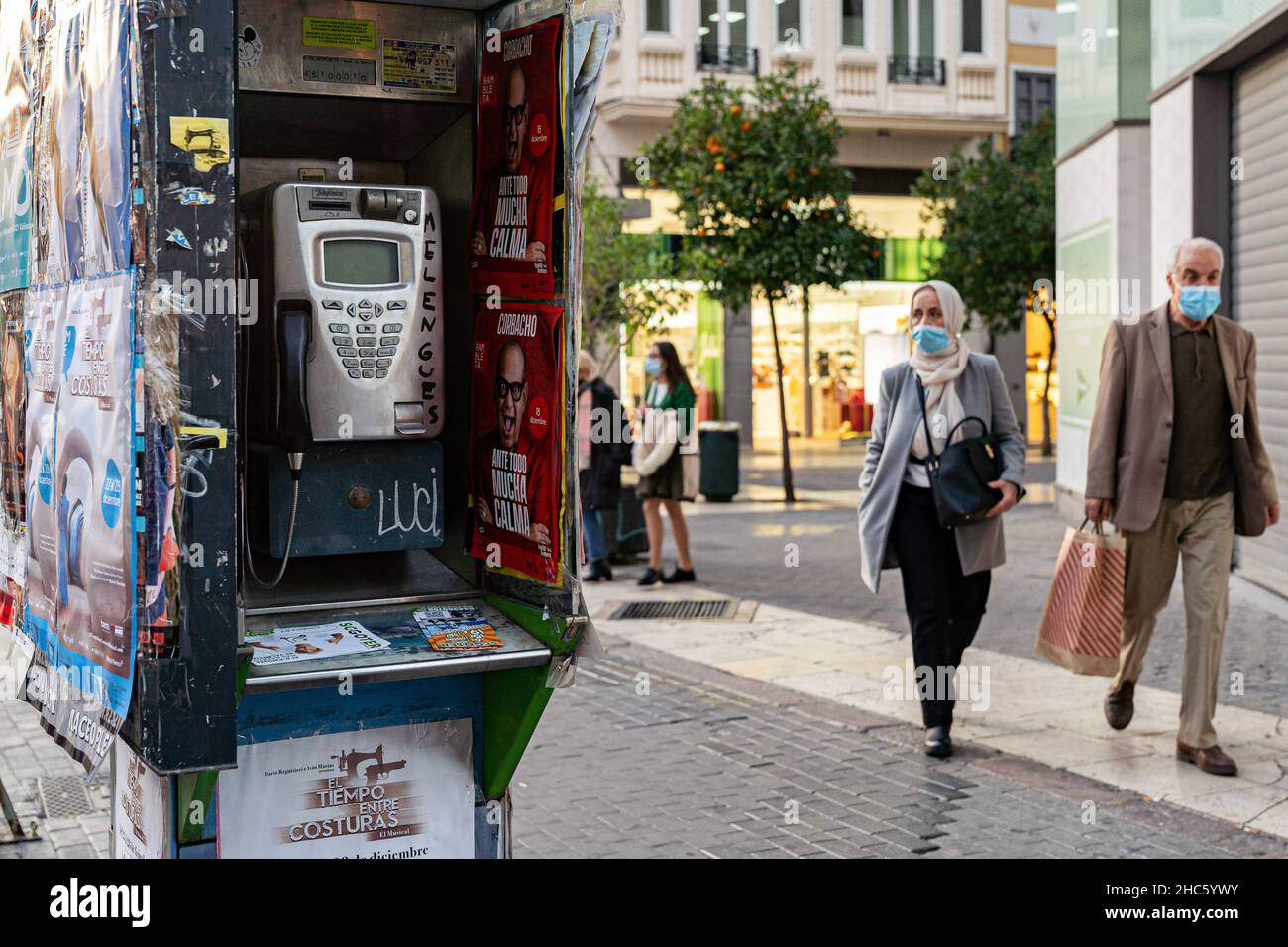 People with masks pass a phone booth in Valencia. According to the new General Telecommunications Law (LGT), phone booths will disappear in 2022. The appearance of the mobile phone has been the main cause of the disuse of these booths. (Photo by Xisco Navarro / SOPA Images/Sipa USA) Stock Photo