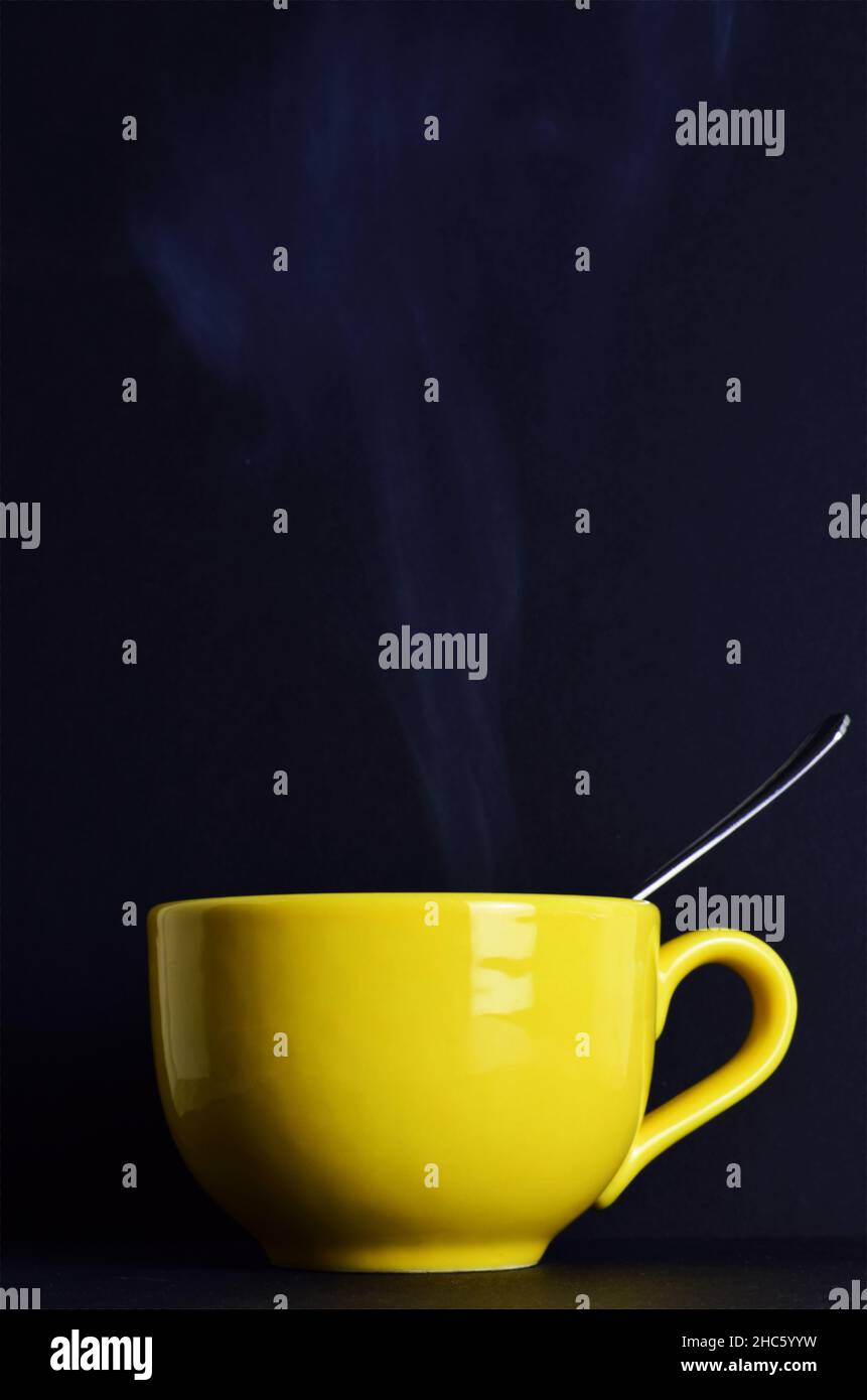 A vertical shot of a spoon in a big yellow mug on a black background Stock Photo