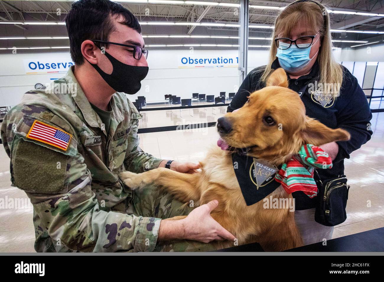 December 9, 2021 - Mt. Laurel Township, New Jersey, USA - U.S. Army Pfc. Daniel Croce with the 1-114th Infantry Regiment, 44th Infantry Brigade Combat Team, New Jersey Army National Guard, pets Logan, a therapy dog, at the newly opened Burlington County COVID-19 Vaccine Mega-Site, Mt. Laurel Township, N.J., Dec. 9, 2021. The Citizen-Soldiers are assisting in temperature screening, inputting insurance information, guiding individuals through the various stations, and monitoring people after they received their vaccinations. (Credit Image: © U.S. National Guard/ZUMA Press Wire Service/ZUMAPRESS. Stock Photo