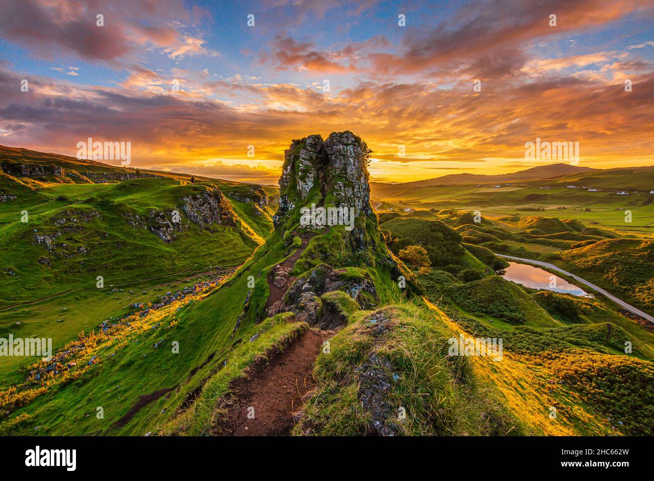 Sunset on the Isle of Skye in Scotland. Castle Ewen mountain hill with paths and meadow in the evening. Red and orange clouds in the sky. small lake w Stock Photo