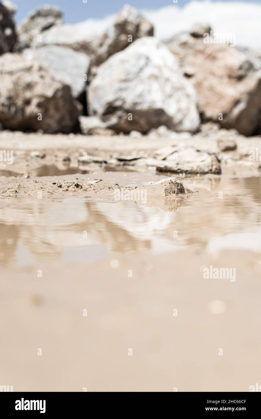 Vertical shot of wet sand on the beach with huge rocks in the ...