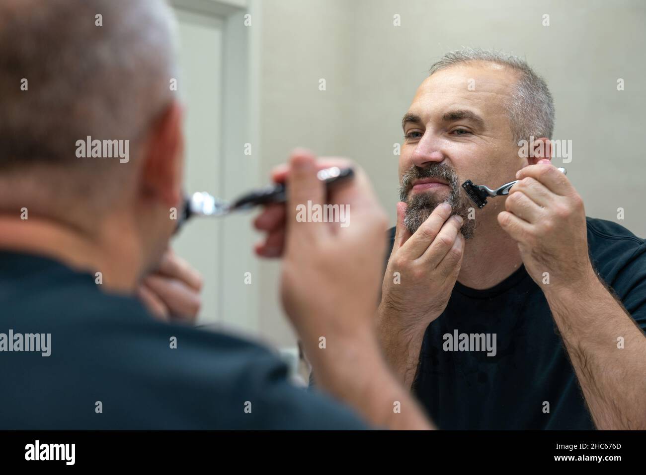 Serious handsome man looking in mirror and shaving his whiskers Stock Photo