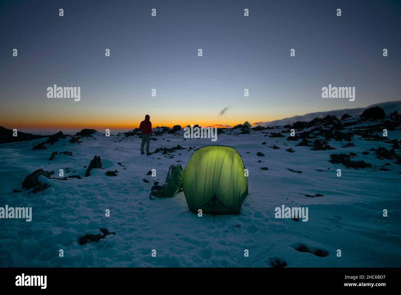 wild camping on the snow of Etna Mountain man and illuminated tent at the  sunset, Sicily Stock Photo