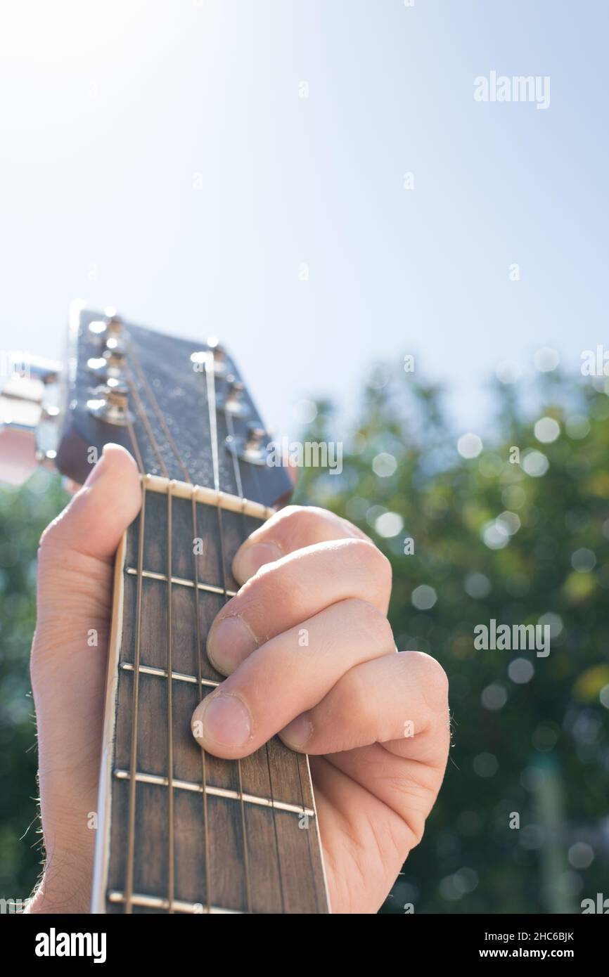 Selective focus of a hand holding an acoustic guitar outdoors, with the sky and greenery in the background Stock Photo