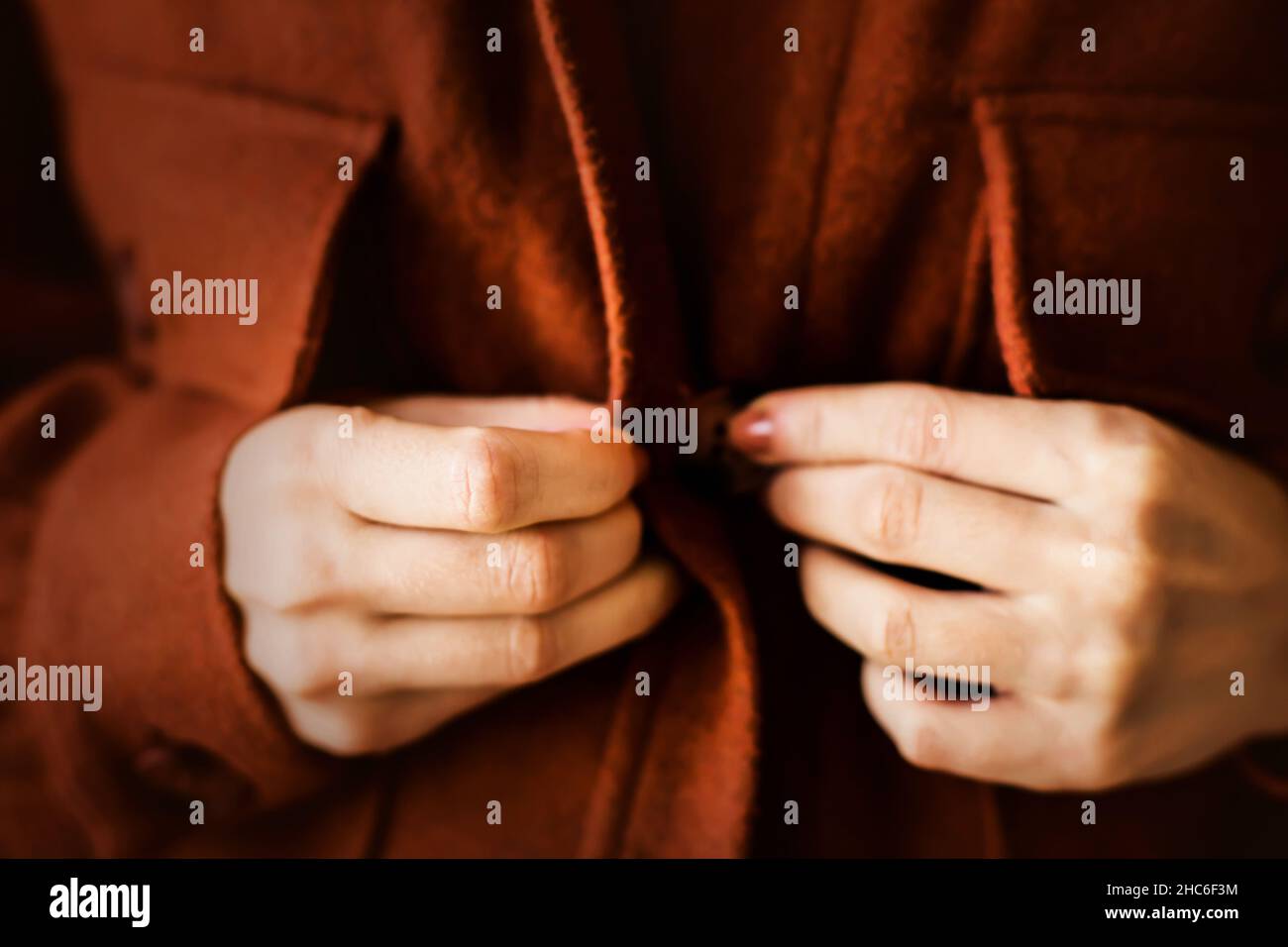 A woman with a brown manicure, dressed in a ginger warm cozy shirt, is buttoning her buttons. Casual fashionable clothes for the autumn season. Soft f Stock Photo