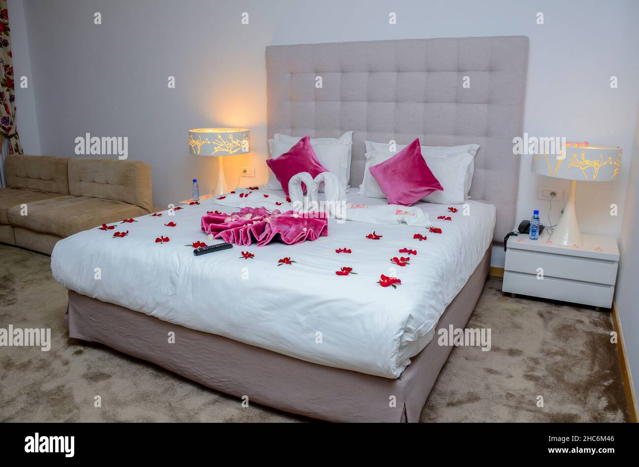 Swan towel decorations and heart shaped rose petals on bed in honeymoon suite hotel room bed Stock Photo