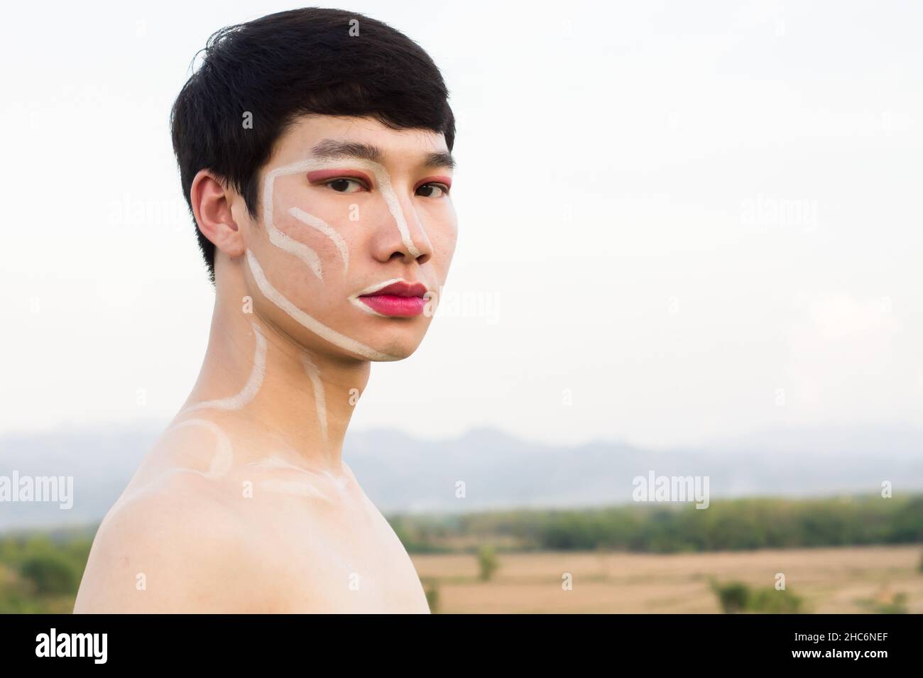 One Asian gay handsome man not wearing a shirt, he writes on the face and wears pink lipstick and pink eye shadow. Copy space Stock Photo