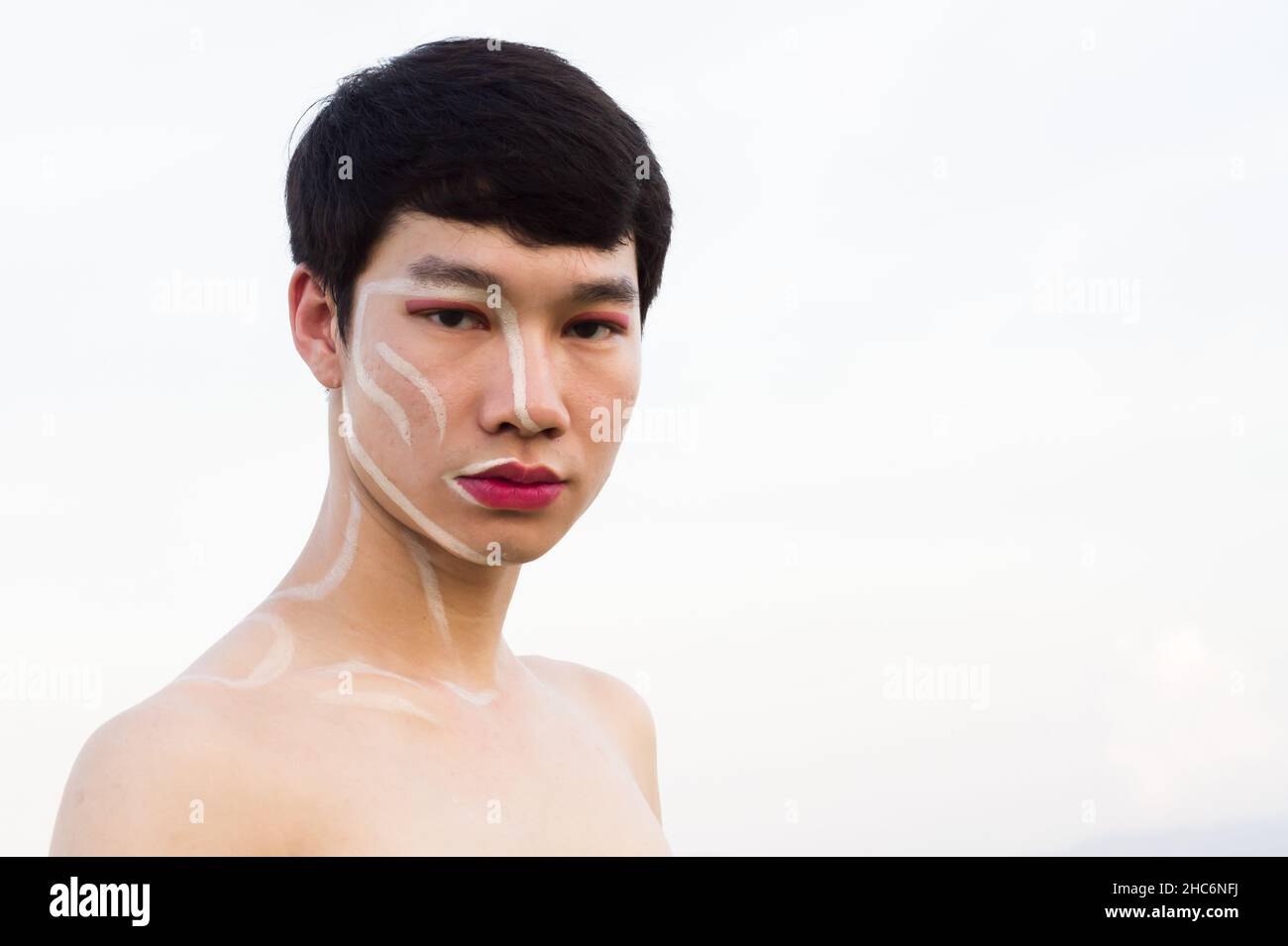 One Asian gay handsome man not wearing a shirt, he writes on the face and wears pink lipstick and pink eye shadow. Copy space Stock Photo