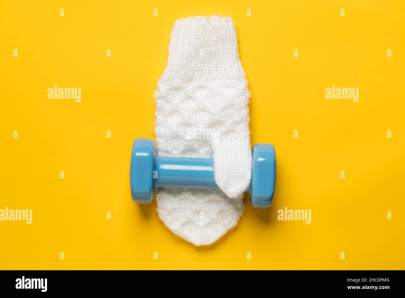 Dumbbell on a white, knitted mitten, on a yellow background. Healthy and active lifestyle concept. Top view.  Stock Photo