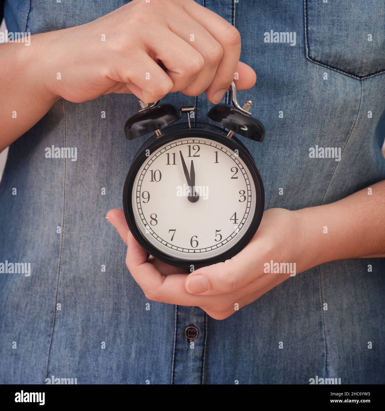 A woman holding an alarm clock that is showing a few minutes before twelve in her hands. Few minutes before deadline.. Close up. Stock Photo