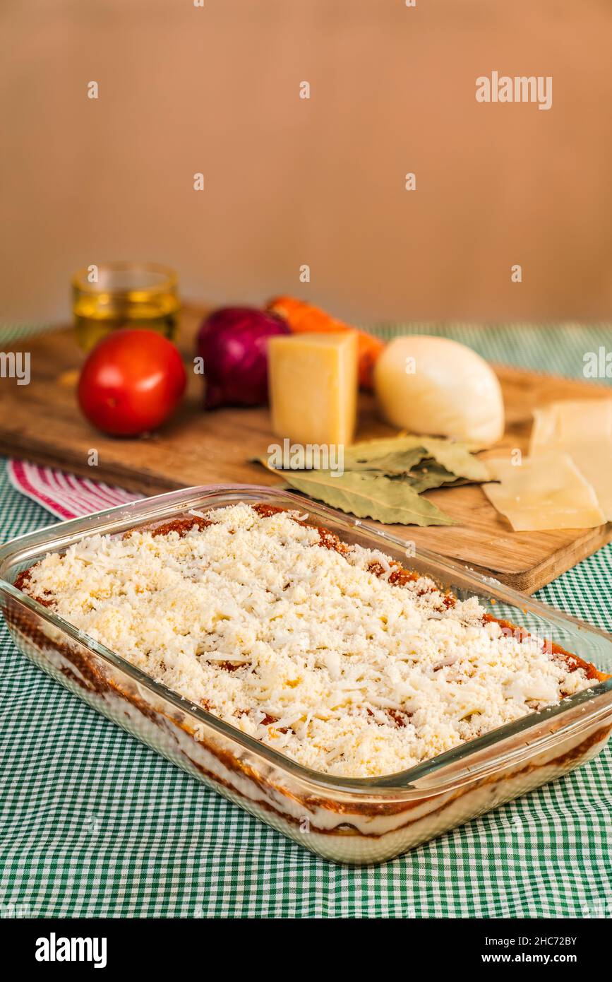 Vertical image of homemade lasagna in a glass tray ready to cook with raw ingredients behind Stock Photo