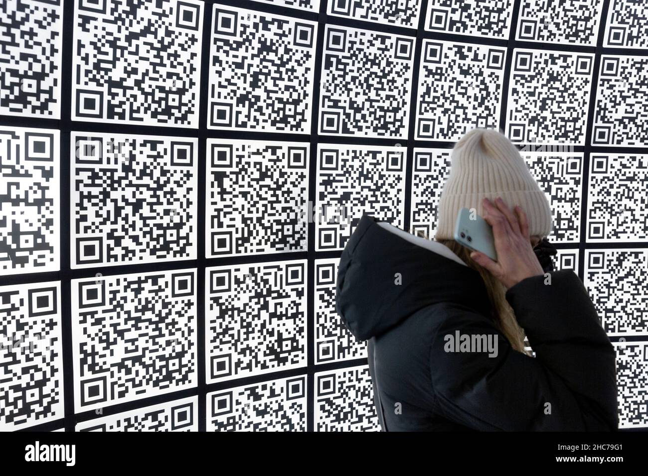 Moscow, Russia. 25th December, 2021 A girl walks in the information center of Moscow against the background of QR codes, Russia Stock Photo