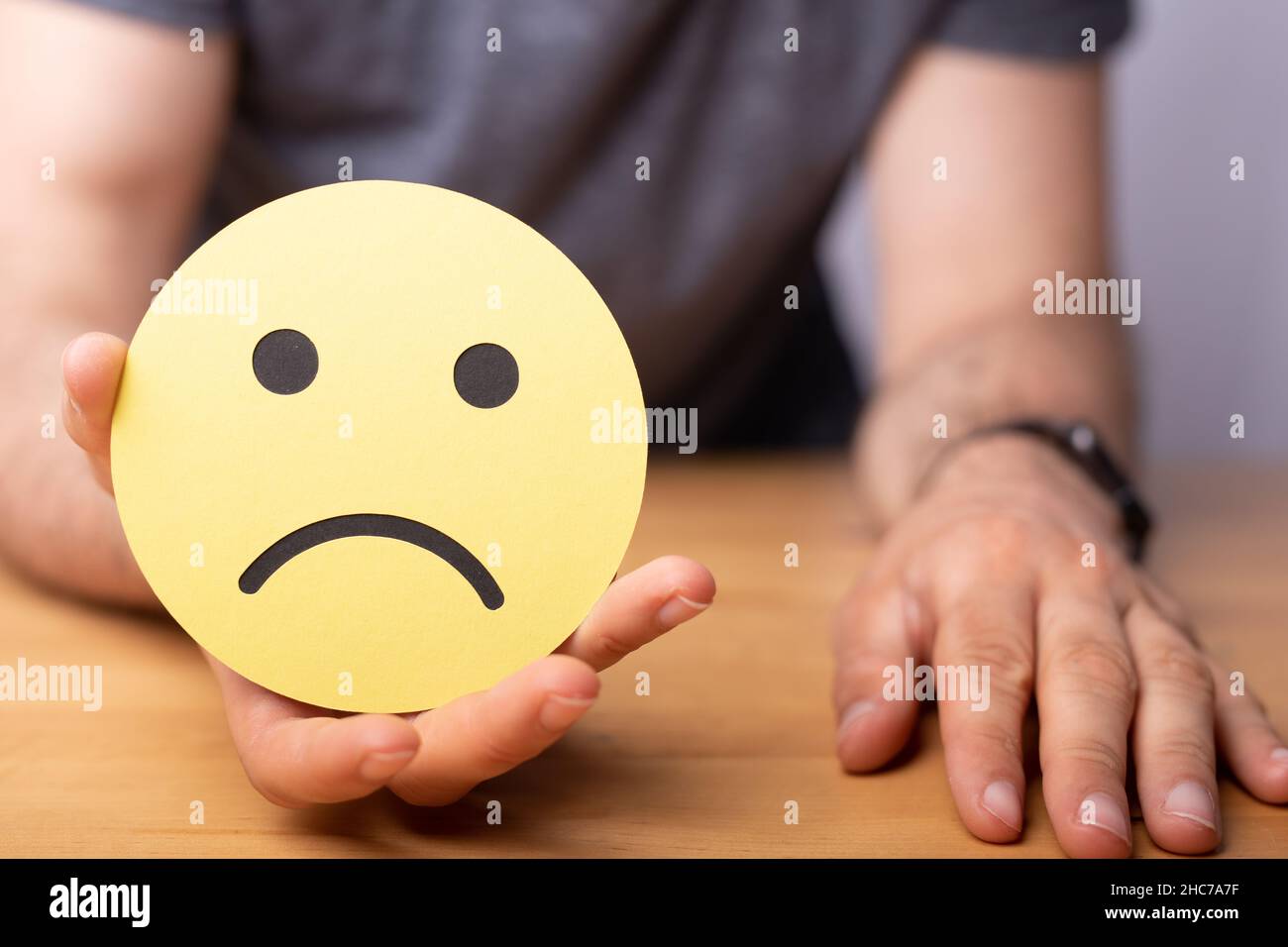 Close-up shot of a hand holding a sad expression emotion smiley on a yellow paper Stock Photo