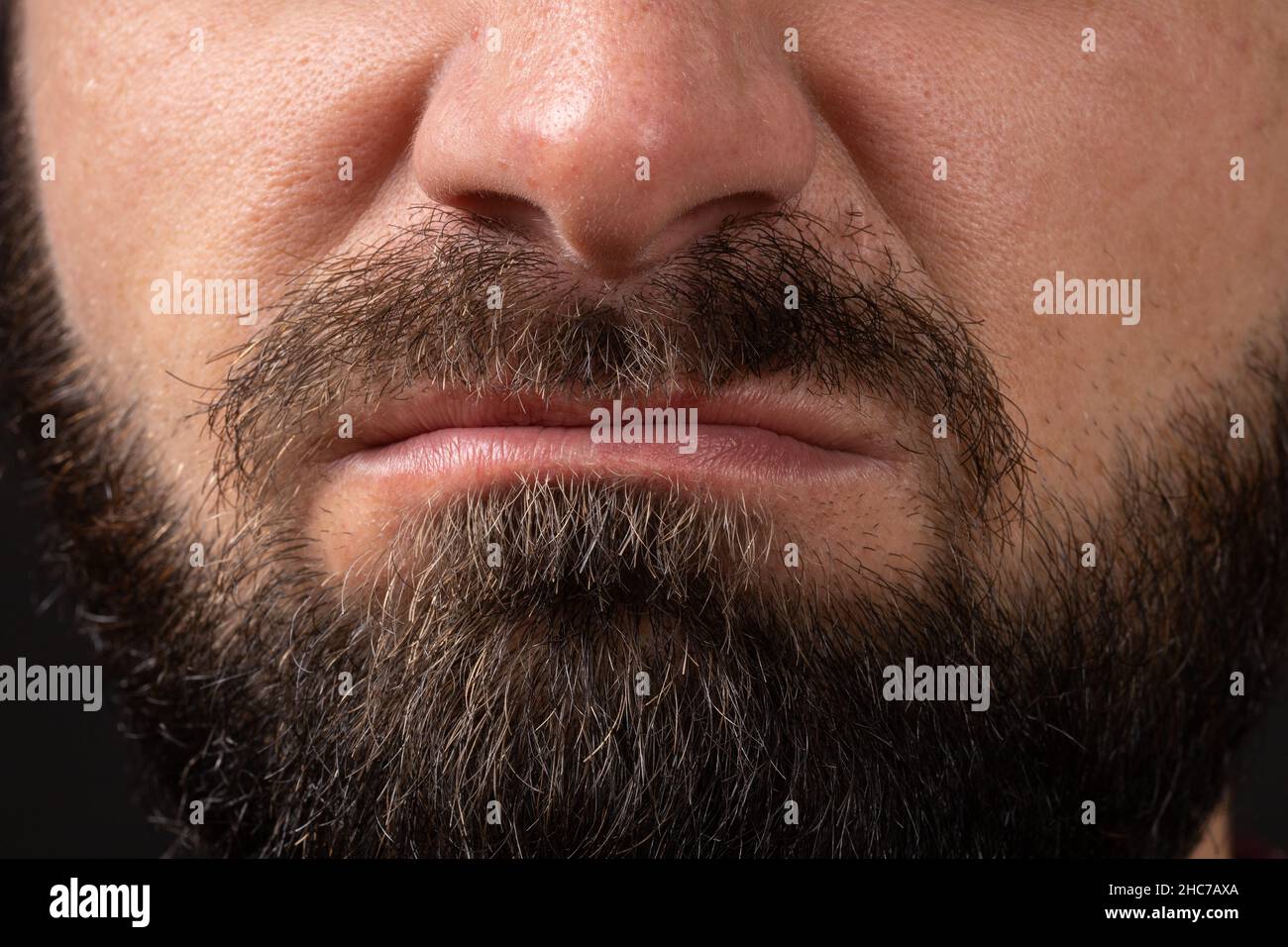 emotion of disgust, hatred close-up on face and lips of young unrecognizable man with black beard and mustache, concept of rage and anger Stock Photo