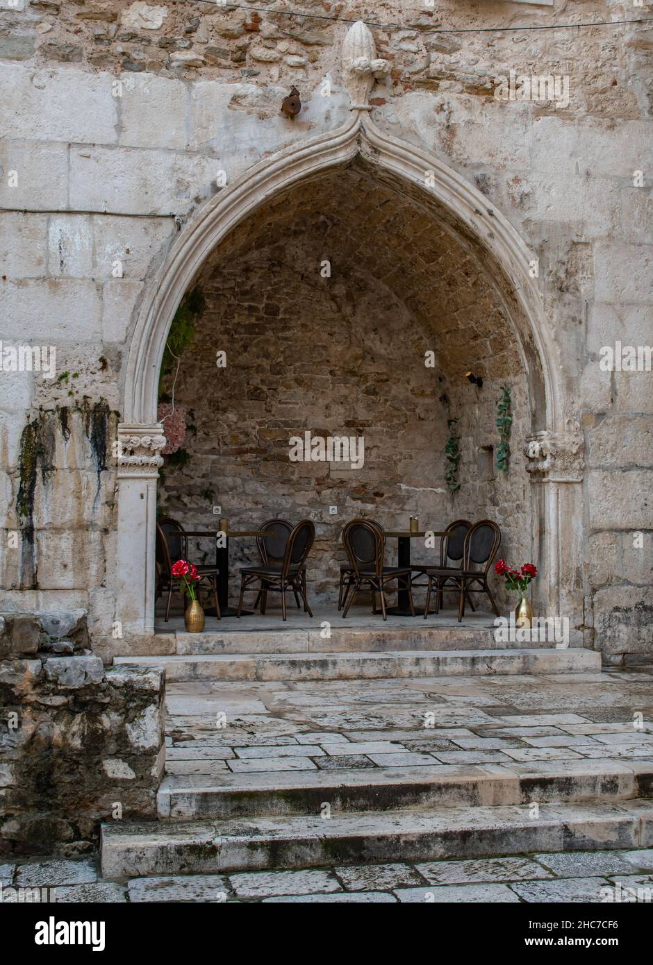 Romantic outdoor dining experience among the ancient architecture- Split, Croatia. Tables and chairs set up in an alcove carved into stone Stock Photo