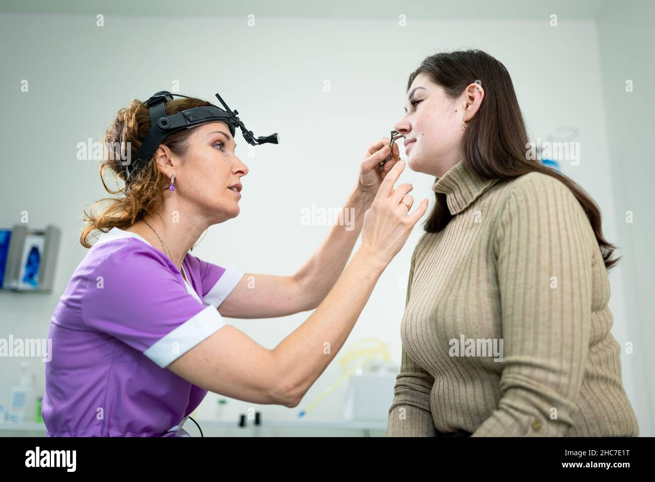 Professional female doctor otorhinolaryngologist doing nose examination with otoscope in modern