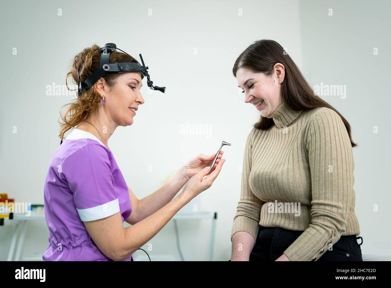 Professional female doctor otorhinolaryngologist doing nose examination with otoscope in modern