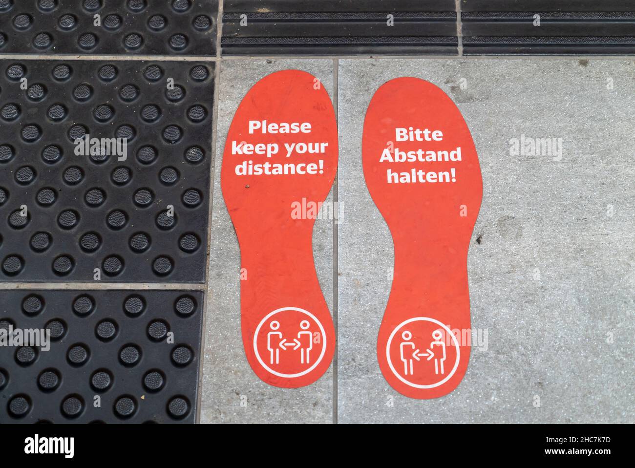 Footstep stickers with a text 'Please keep your distance' on the ground during pandemic Stock Photo