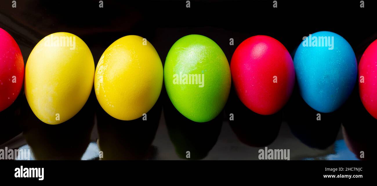 Bright, multi-colored eggs lie in a row on a rectangular black ceramic dish. Easter. Minimalism. Stock Photo