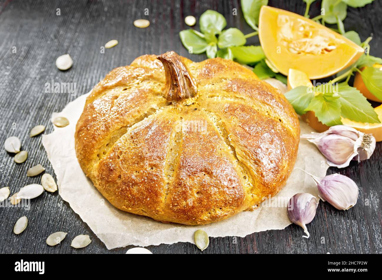 Pumpkin bread on parchment, garlic, basil, pieces and seeds of a vegetable on a wooden board background Stock Photo