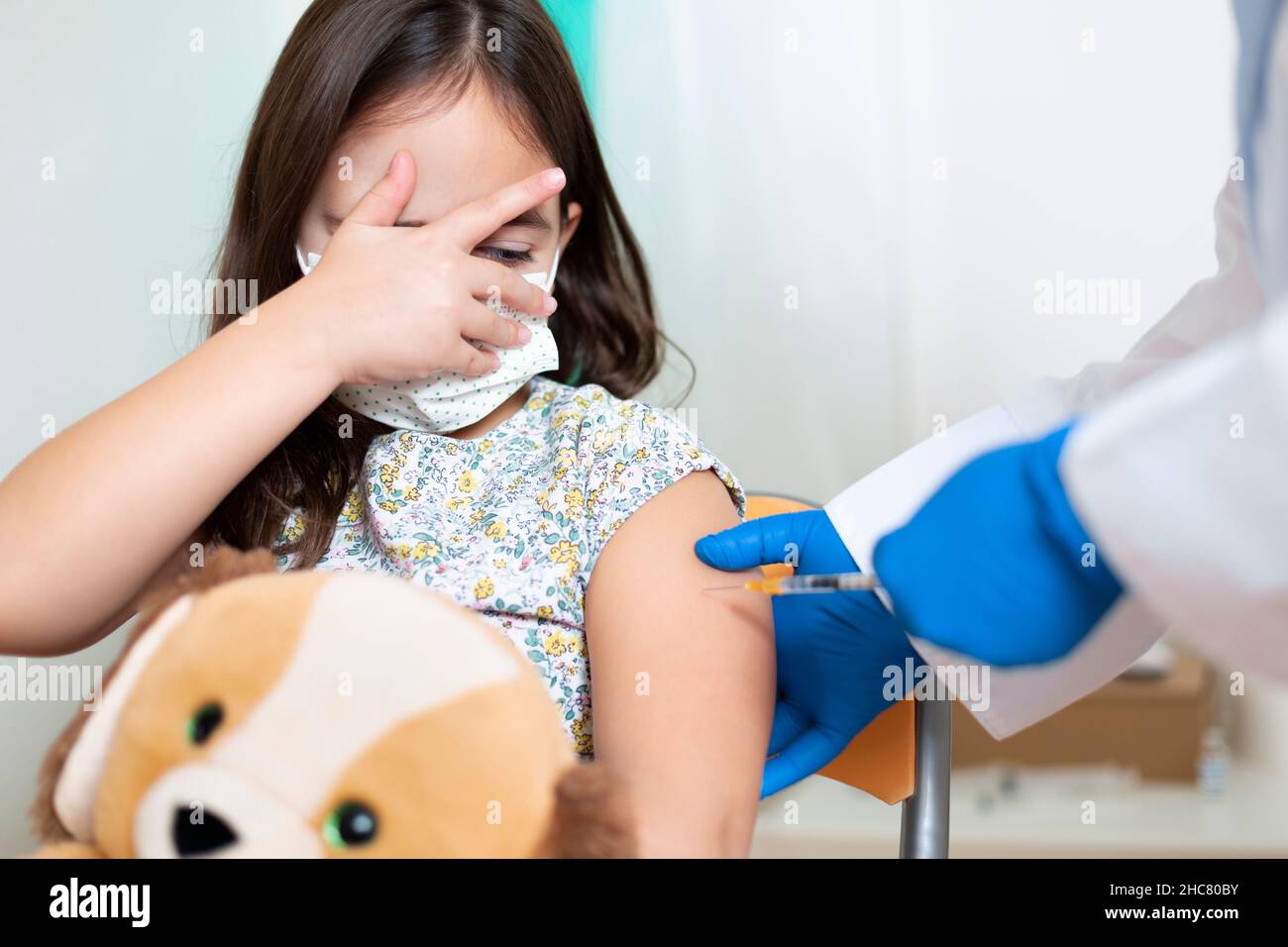 Fearful little Caucasian girl receiving a dose of Coronavirus vaccine. Childhood vaccination concept. Stock Photo