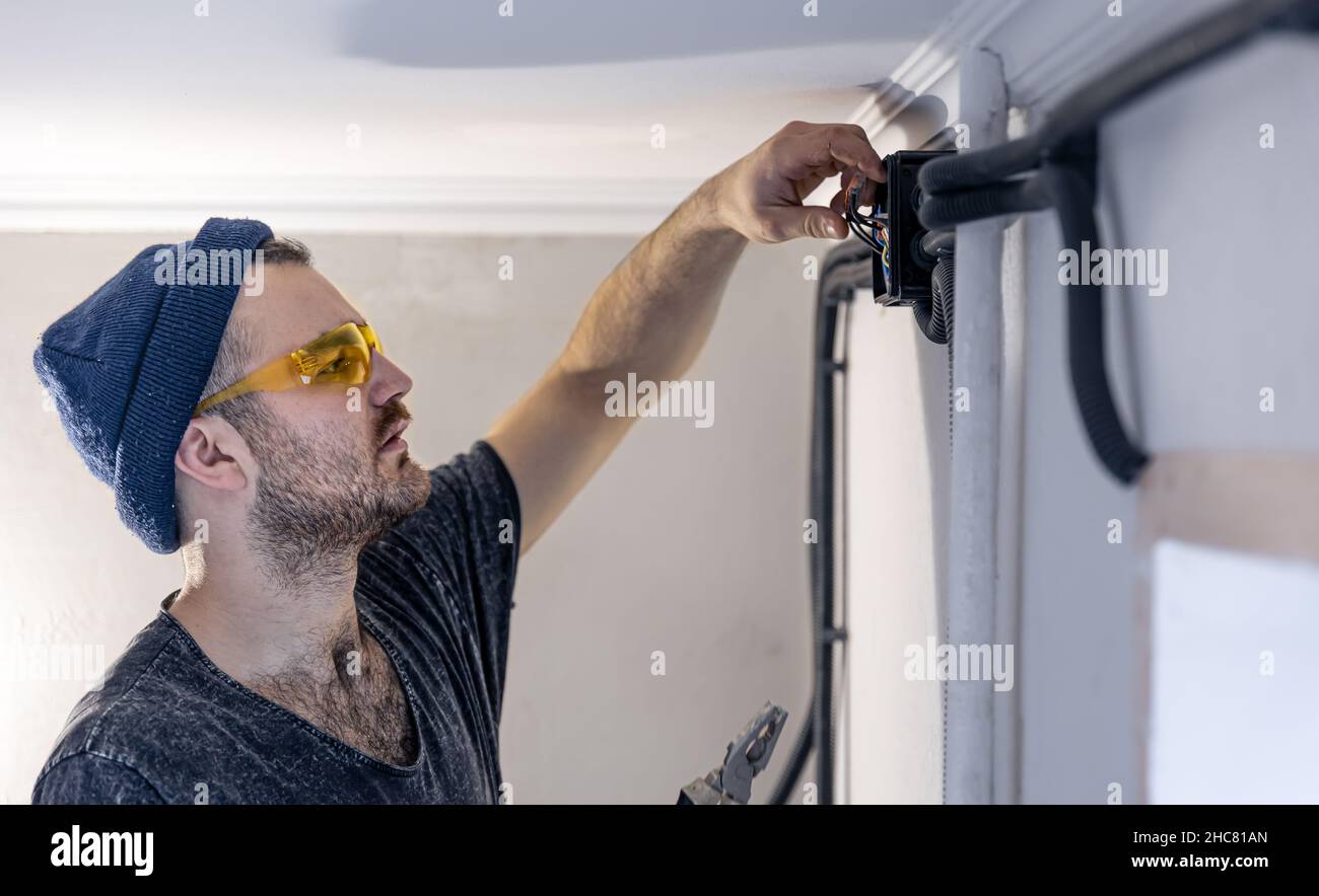 An electrician is mounting electric sockets on the white wall indoors. Stock Photo