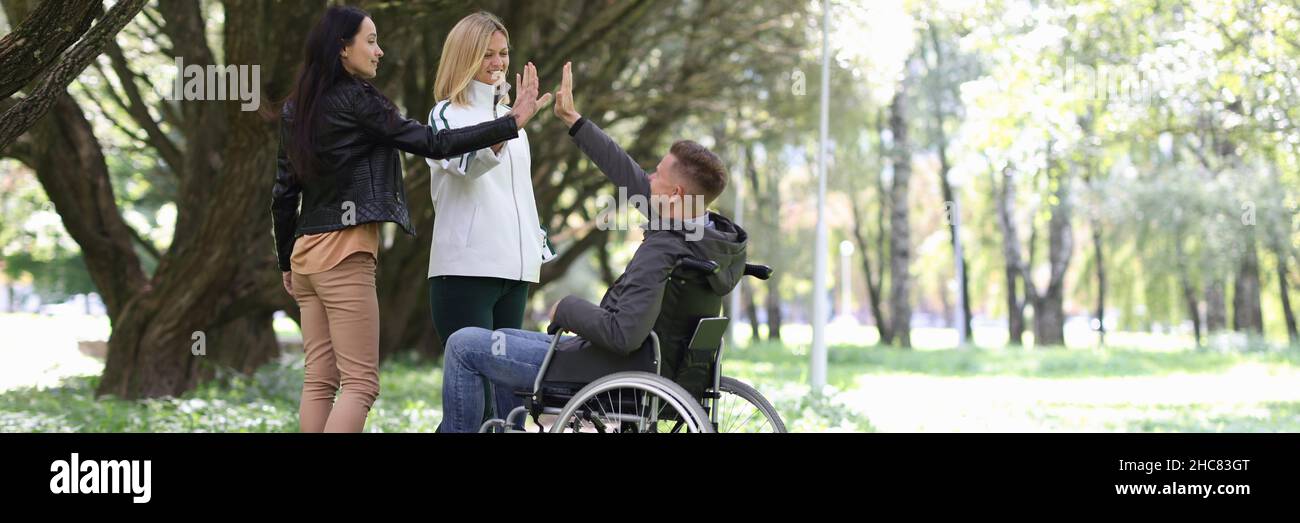 Man in wheelchair giving five to female friends in park Stock Photo - Alamy