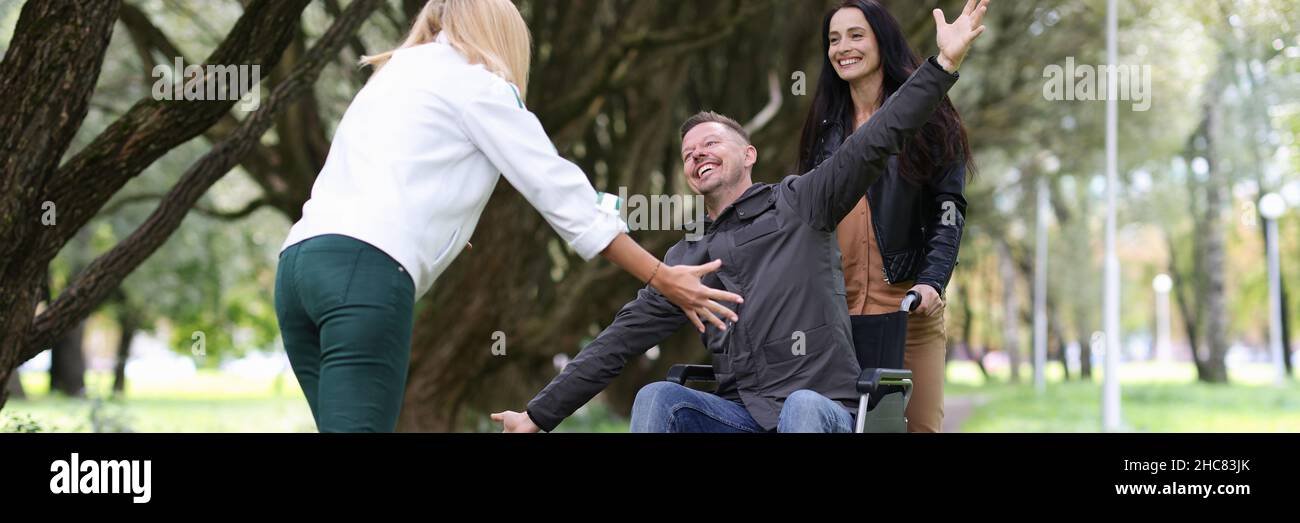 Man in wheelchair walking in park with nurse and hugging his girlfriend ...