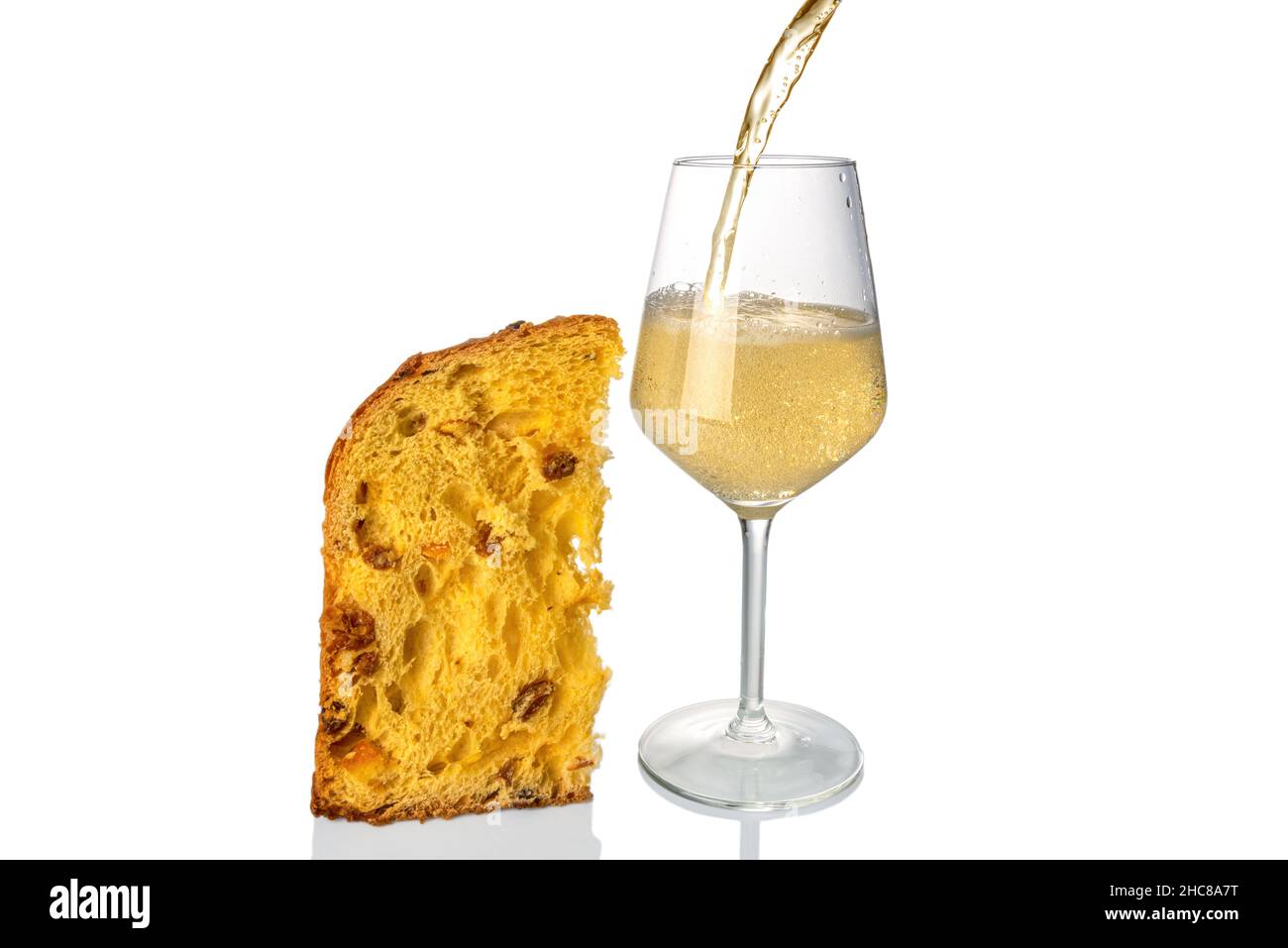 Champagne or sparkling wine splashing into glass with slice of panettone cake, isolated on white, Christmas or New Year celebrations concept, copy spa Stock Photo