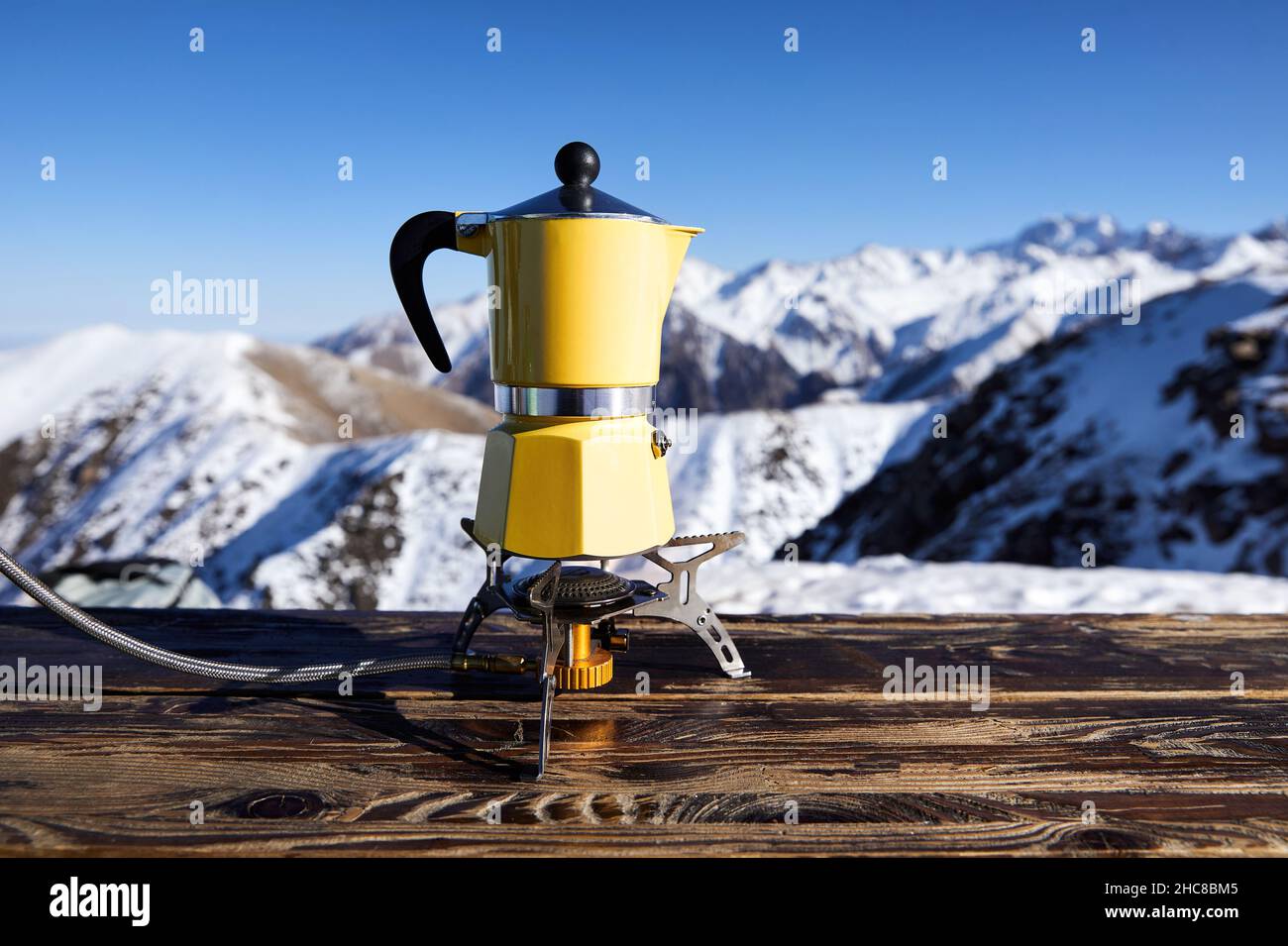 Yellow moka pot coffee at snow mountain camping. Morning picnic, person cooking hot drink for breakfast in nature. Stock Photo