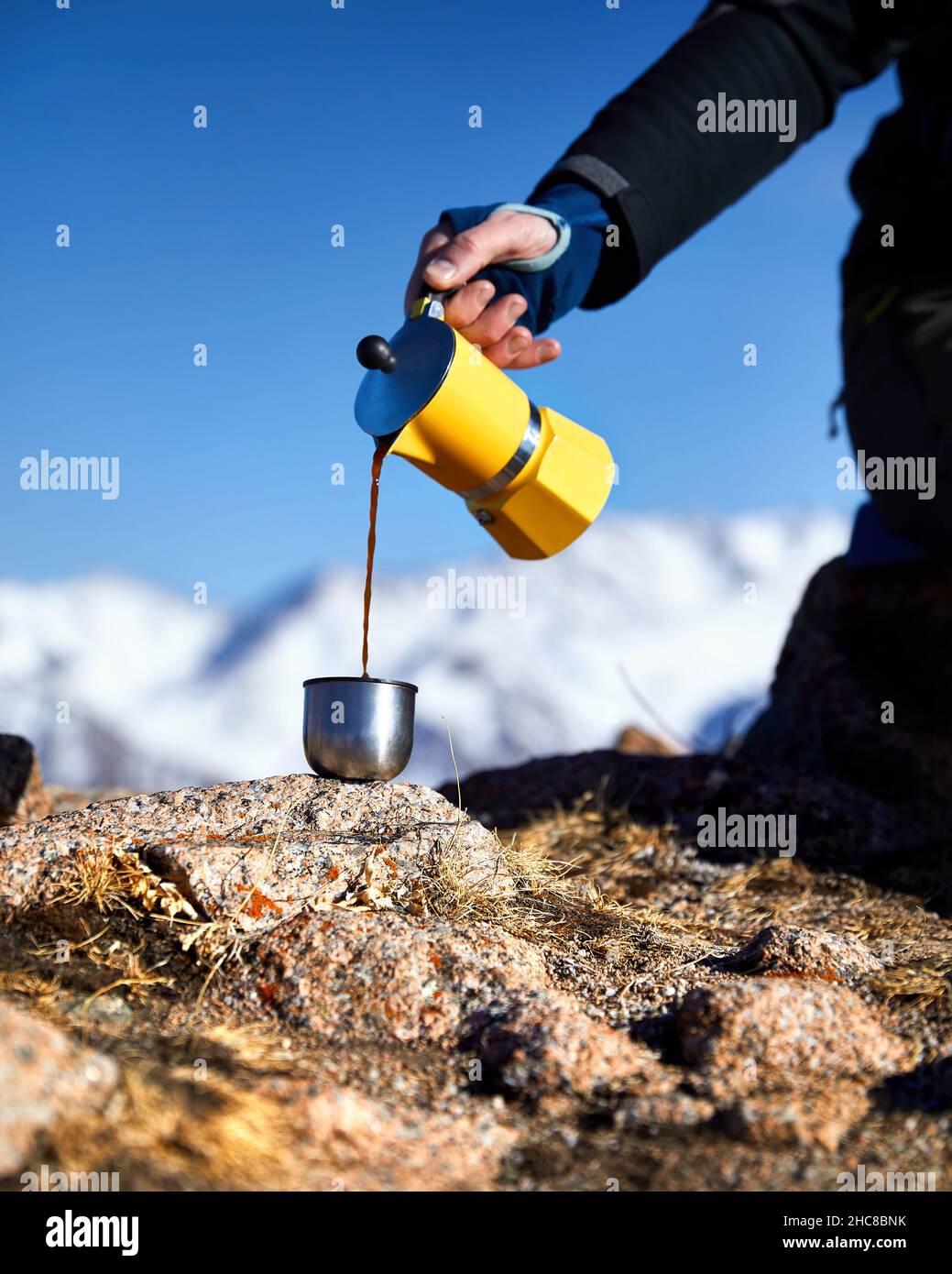 Man hiker pouring coffee from Yellow Moka mocha pot outdoors in the snow winter mountains. Old style coffee vintage pot outdoor camping Stock Photo
