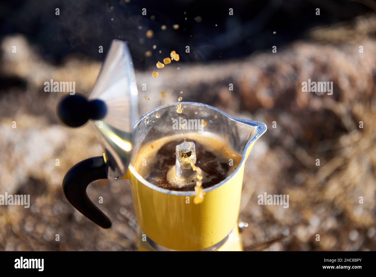 Yellow Moka coffee pot on stove on table with open cover with brown hot beverage splash drop. Old style coffee vintage pot outdoor camping Stock Photo