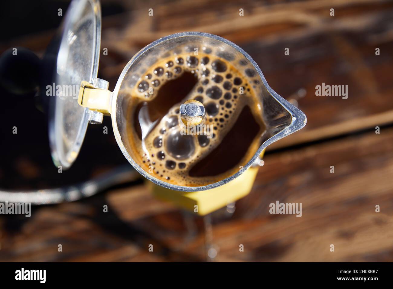 Yellow Moka coffee pot on stove on table with open cover with brown hot beverage inside. Old style coffee vintage pot outdoor camping Stock Photo
