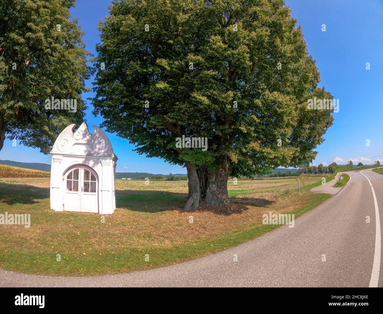 Beautiful shot of a chapel in an idyllic location between two trees on the side of the path Stock Photo