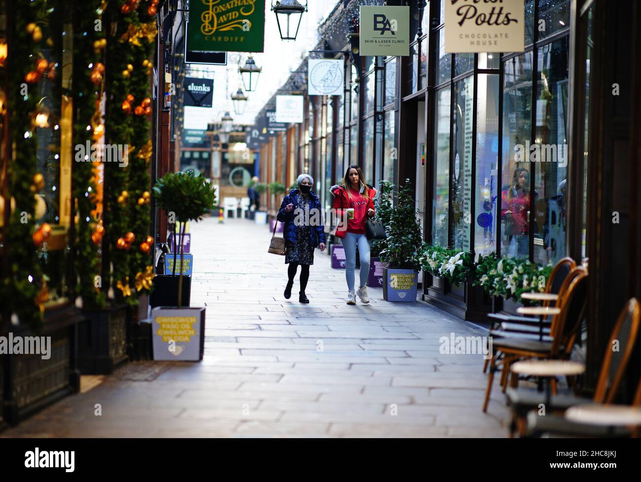 Two women walk through a shopping arcade in the centre of Cardiff, Wales, as new Covid-19 rules come into force. Groups of no more than six people will be allowed to meet in pubs, cinemas and restaurants in Wales, with two-metre social distancing being required in public premises and offices. Picture date: Sunday December 26, 2021. Stock Photo