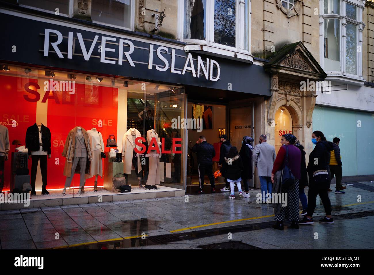 People stand in line to enter a branch of River Island in Cardiff, Wales, as new Covid-19 rules come into force. Groups of no more than six people will be allowed to meet in pubs, cinemas and restaurants in Wales, with two-metre social distancing being required in public premises and offices. Picture date: Sunday December 26, 2021. Stock Photo