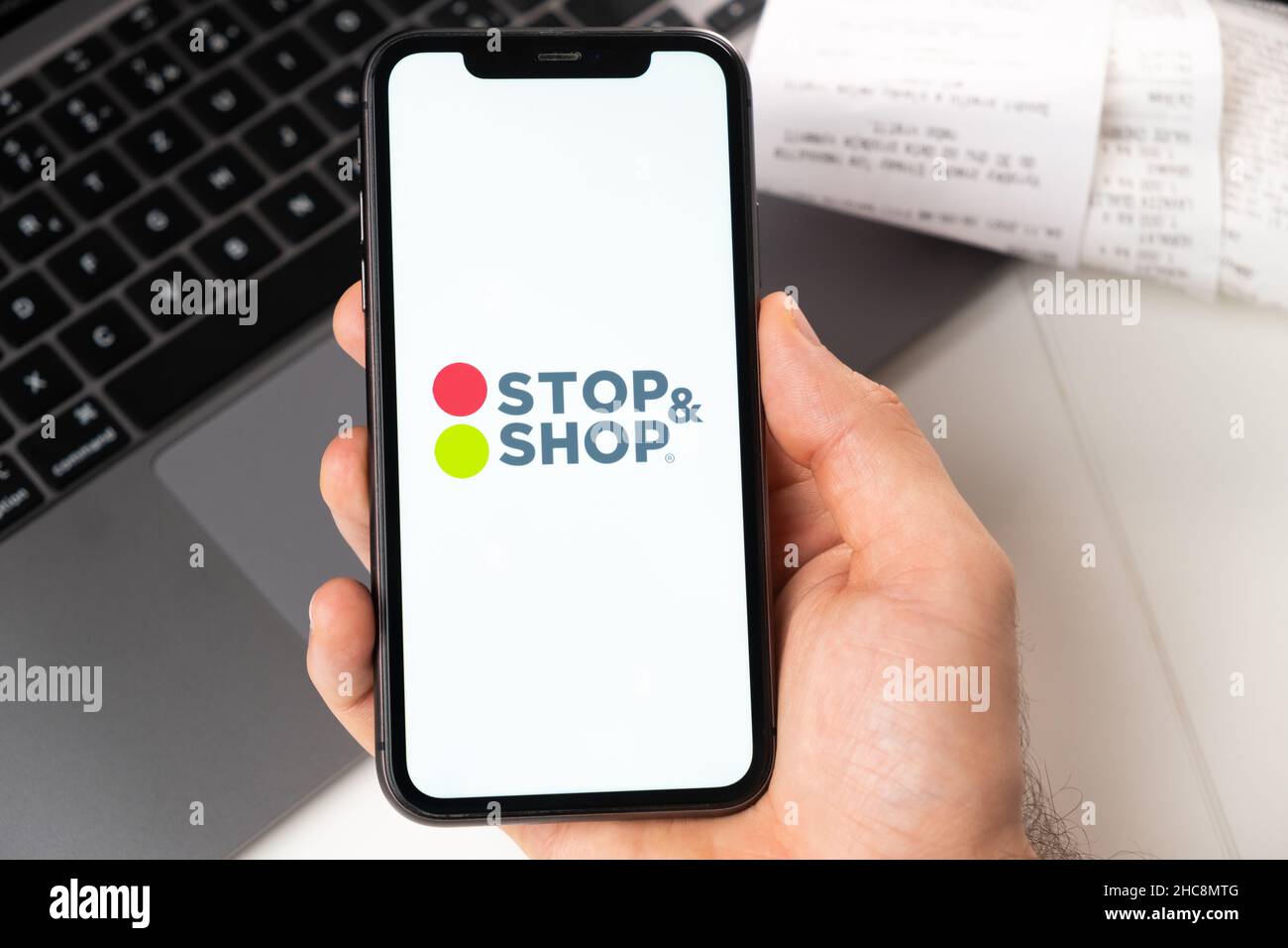 Stop and shop application on the screen of Apple iPhone in mans hand and laptop on the background. Online shopping concept. November 2021, San Francisco, USA Stock Photo