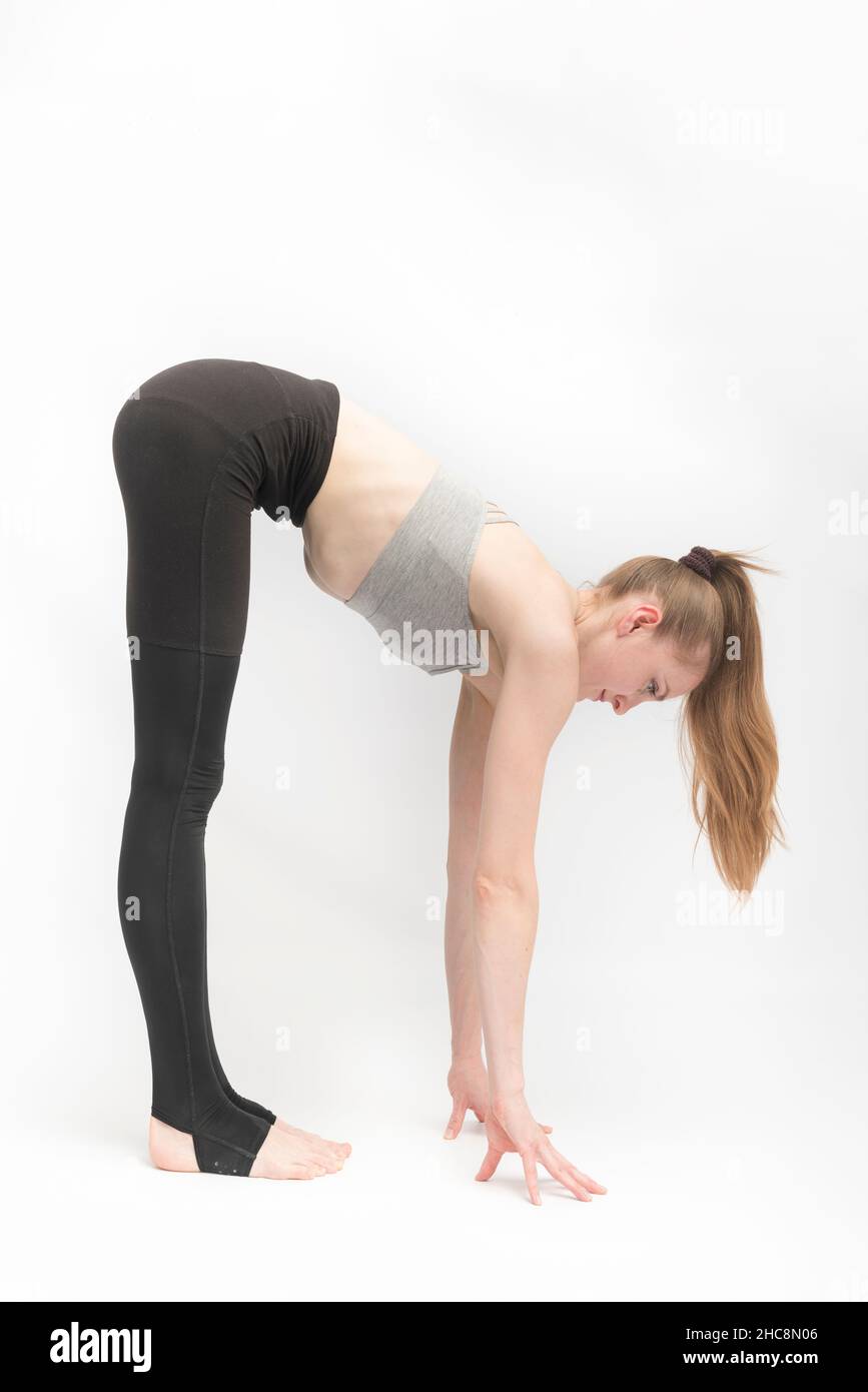 Young woman in tight leggings and top is doing stretching. Girl reaches for  the floor with her hands on white background. Exercise for flexibility  Stock Photo - Alamy