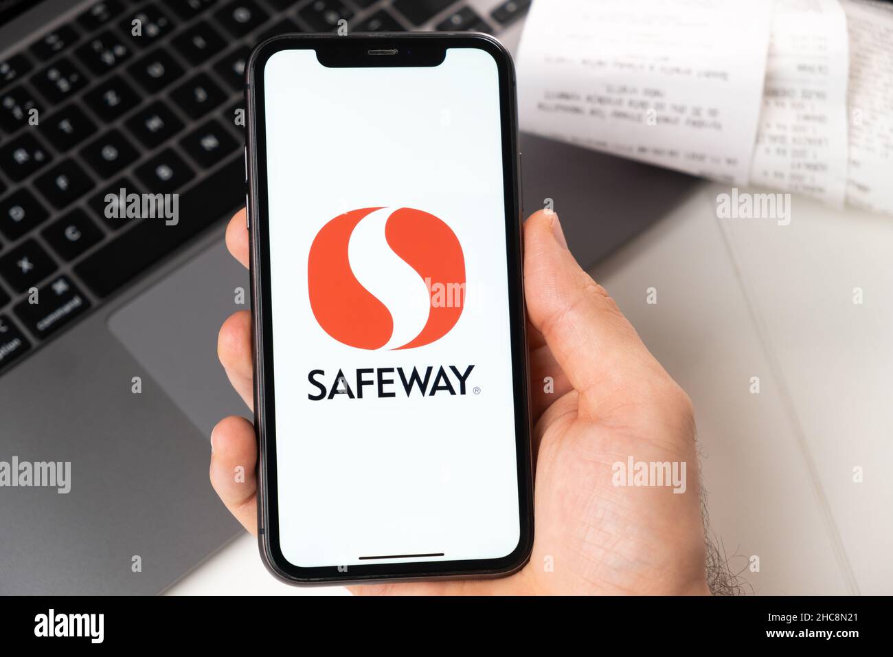 Safeway application on the screen of Apple iPhone in mans hand and laptop on the background. Online shopping concept. November 2021, San Francisco, USA Stock Photo