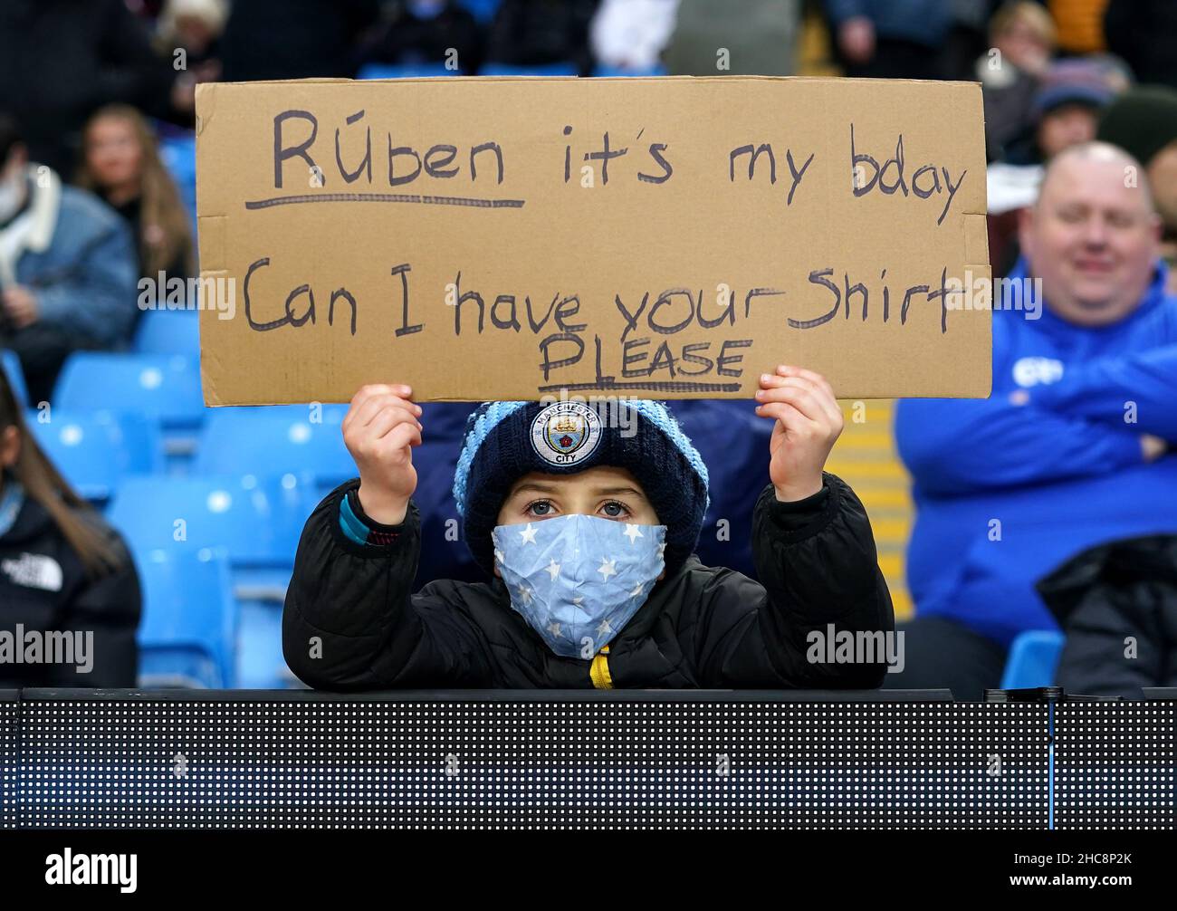A young Manchester City fans with a face masks on holds up a sign for
