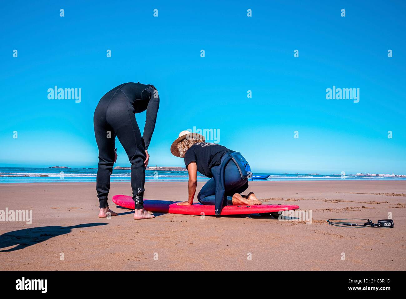 Male instructor demonstrating how to stand up on surfboard to man Stock