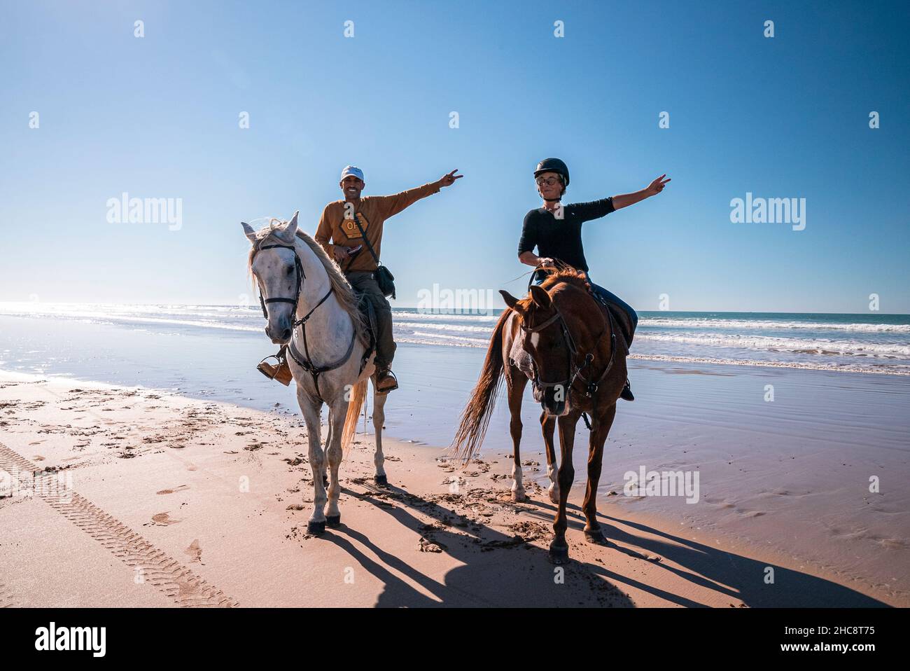 Man and woman showing victory hands gestures while sitting on horses at beach Stock Photo