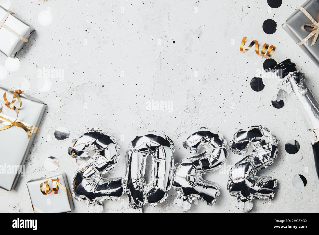 New Year 2022 gray background flat lay. Top view on 2022 balloon silver metallic numbers with confetti, grey gift boxes. Invitation or greeting card concept. Festive mood. Bottle of champagne bottle Stock Photo