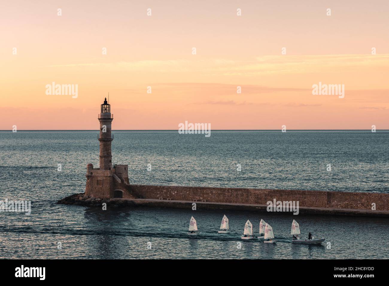 Orange sky at sunset with sailboats at the lighthouse of the Venetian port in old town of Chania - Crete Island, Greece Stock Photo
