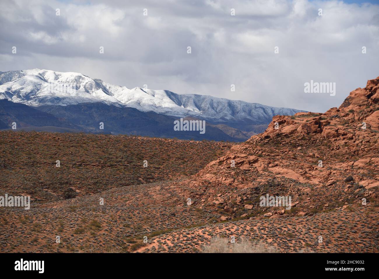A large format panoramic Winter landscape contrasting a red desert rocky valley with distant snow covered mountains.  Shot in Southern Utah, USA. Stock Photo