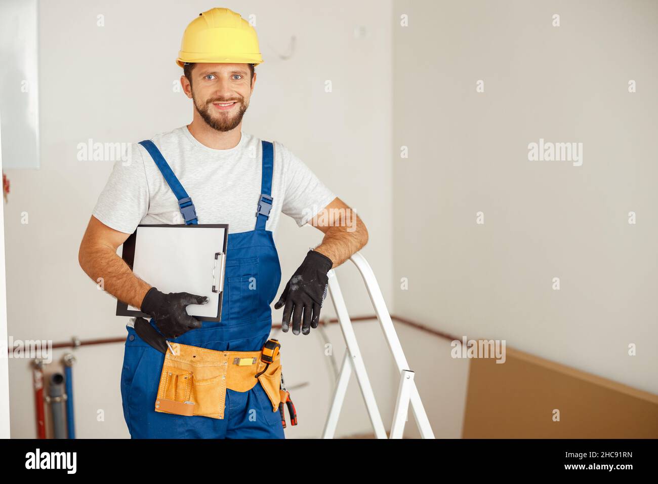 Smiling repairman holding clipboard and smiling at camera while standing in new apartment Stock Photo