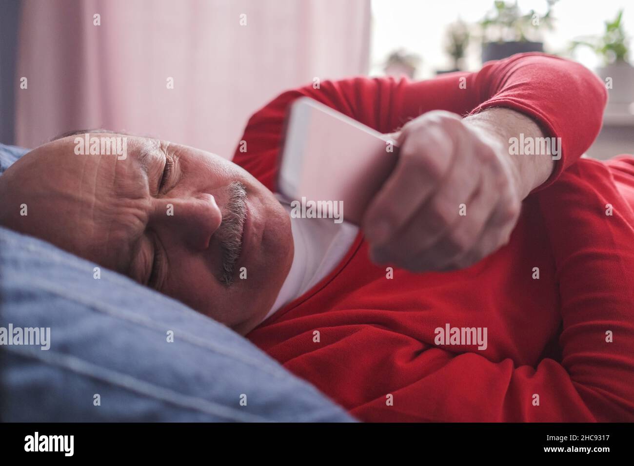Senior caucasian man using smart phone lying on sofa at home. Stock Photo