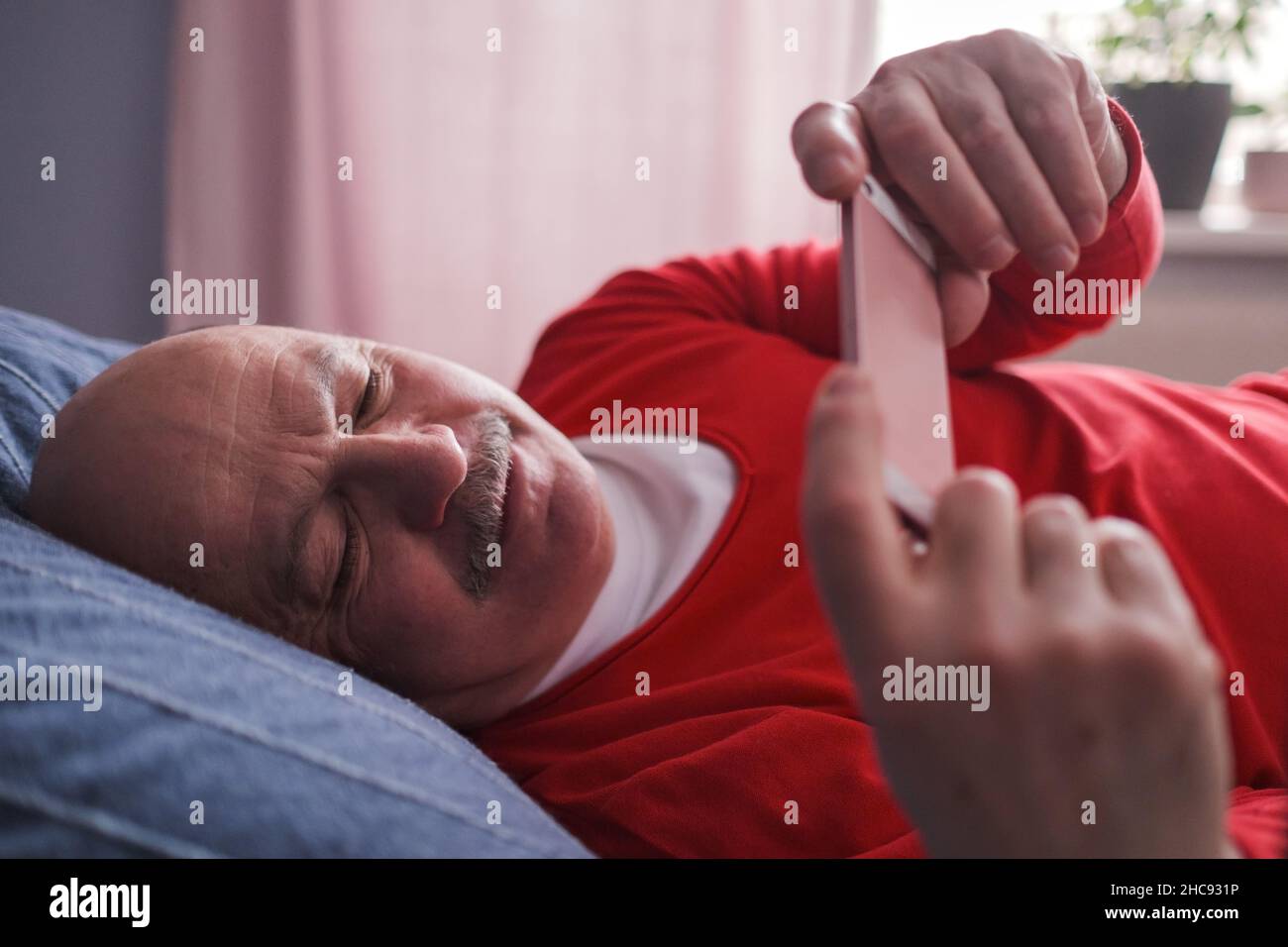 Senior caucasian man using smart phone lying on sofa at home. Stock Photo
