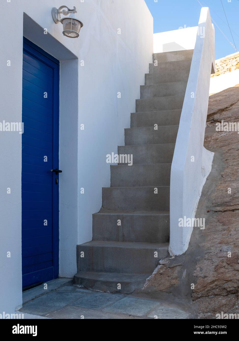 A typical house entrance in the Aegean island of Santorini, Greece, with a blue door and a small staircase and no people. Taken at the end of a sunny Stock Photo
